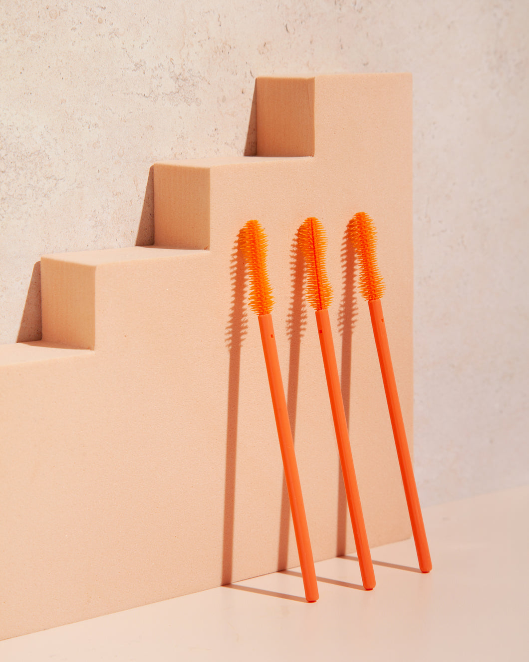 3 orange eyelash wands resting on an orange background